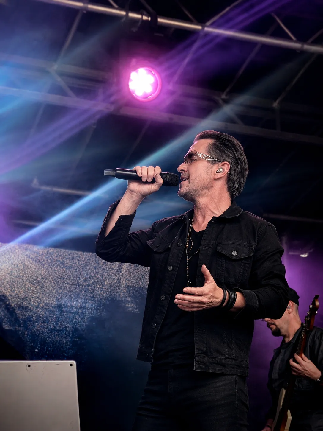 U2.V2 frontman singing into a handheld mic under purple stage lights at the Ultimate Festival, Dumfries