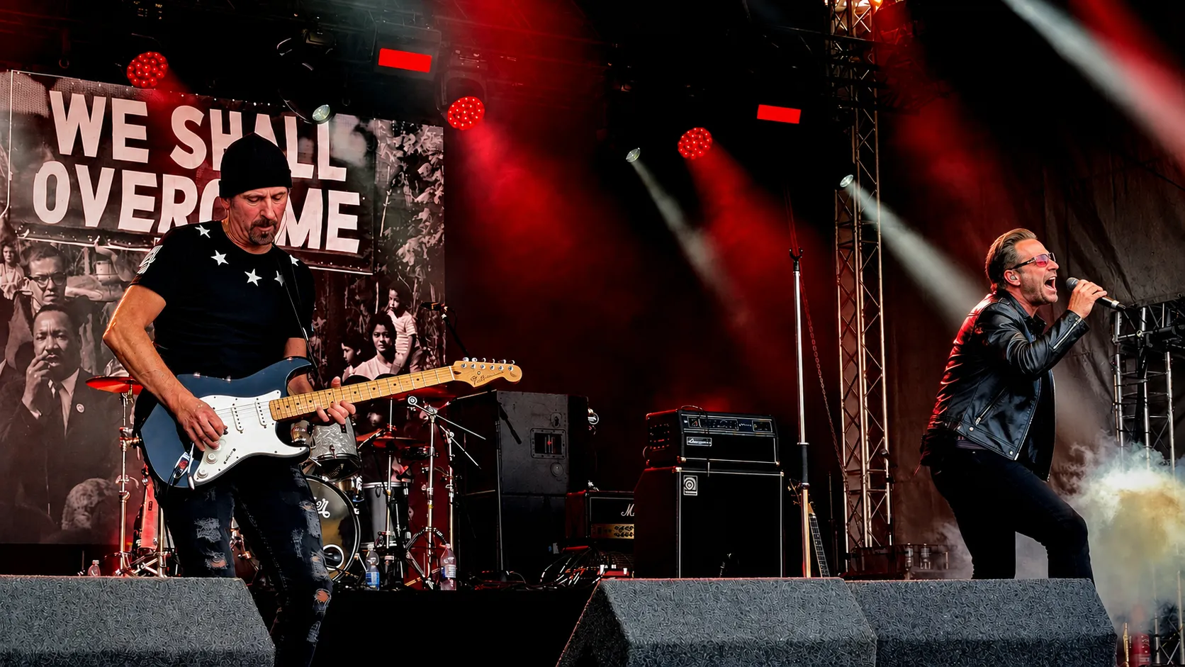 U2.V2 guitarist and frontman on the Tribfest main stage with a We Shall Overcome backdrop under red lights